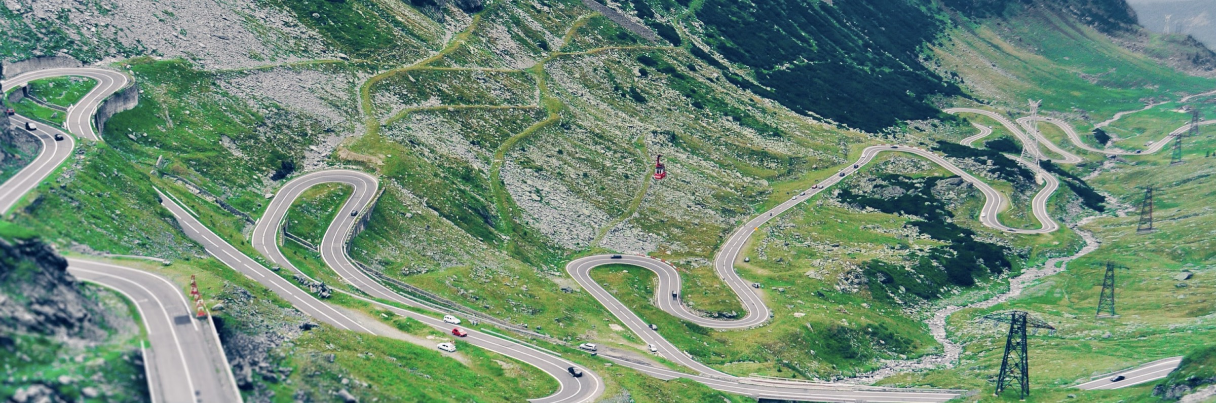 Een bergweg met haarspeldbochten slingert omhoog door een groen dal.